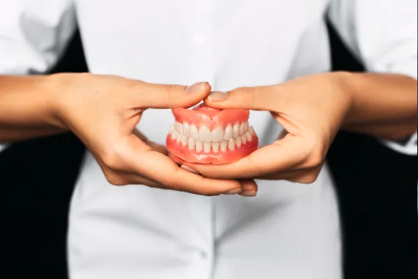 Dentures in Stuart — hand holding a full set of dentures with pink gums and white teeth